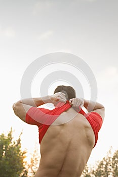 Rear view of muscular man taking off his red shirt in the park in Beijing, China