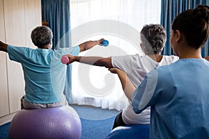 Rear view of nurse training seniors in lifting dumbbells