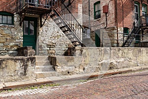 Rear view of old apartment buildings, sidewalk and red brick street, fire escapes and weathered walls and steps