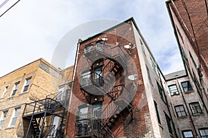 Rear view of old brick apartment buildings with metal fire escapes, windows and doors