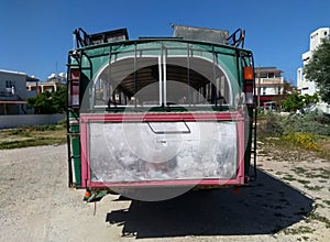 Rear view of an old rusting green painted bus with roof rack parked in a rustic location in cyprus