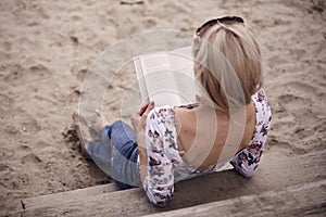 Rear view, one young girl back, laying relaxing on sand steps, reading a book