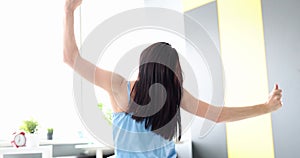 Rear view of optimistic young woman sitting on bed in bedroom