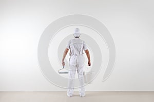 Rear view of painter man looking at blank wall, with paint roller and bucket, isolated on white room