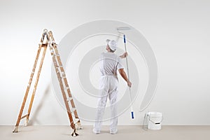 Rear view of painter man looking at blank wall, with paint stick