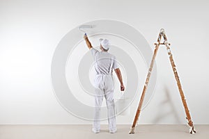 Rear view of painter man painting the wall, with paint roller an