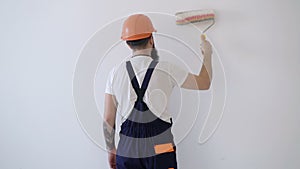 Rear view of painter man painting the wall, with paint roller isolated on big empty space. Concept of repair works. Copy