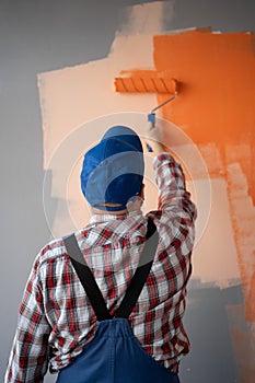 Rear view of a painter painting a wall with a roller of orange paint. Close-up of the back of a worker doing renovations