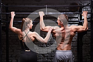 Rear view photo of couple of man and woman in the sportwear making exercise on a horizontal bar against brick wall.