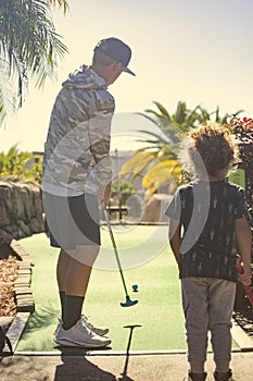 Rear view photo of two boys playing mini golf while on a fun family vacation together.