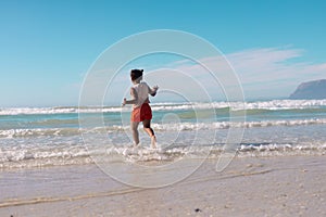 Rear view of playful african american girl running in sea against blue sky on sunny day
