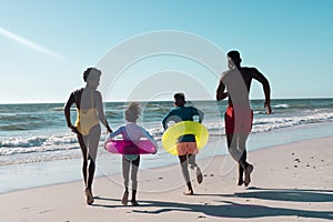 Rear view of playful african american parents and children with swimming floats running towards sea