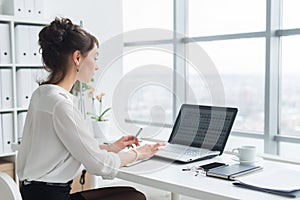 Rear view portrait of a businesswoman sitting on her workplace in the office, typing, looking at pc screen.