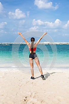 Rear view portrait of fitness woman stretching with her hands raised at the beach