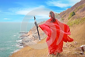 Rear view portrait of young and beautiful woman wearing red Chinese warrior costume with black sword, she post using sword on