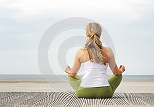 Rear view portrait of young woman sitting at beach in yoga pose