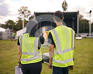 Rear View Of Production Team With Headsets Setting Up Outdoor Stage For Music Festival Or Concert