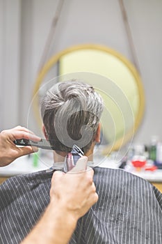 Hairdresser does hairstyle with hair clipper and comb. Barbershop concept