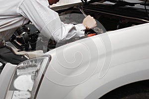 Rear view of professional young mechanic man in uniform with wrench diagnosing engine against car in open hood at the repair garag