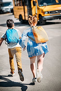 rear view of pupils with backpacks running to