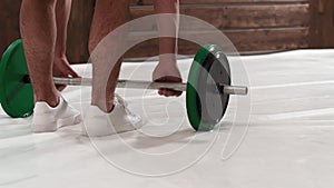 Rear view. With ray of light weightlifting young man bent gripping a black and green weight set, equipment for weight