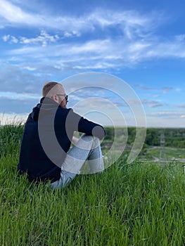 Rear view of relaxed young man sitting on grass against blue sky.