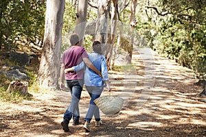 Rear View Of Romantic Couple Hiking Along Forest Path