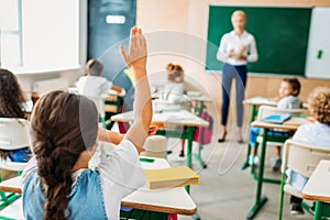 rear view of schoolgirl raising hand to answer teachers question