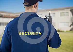 Rear view of security guard using radio against house