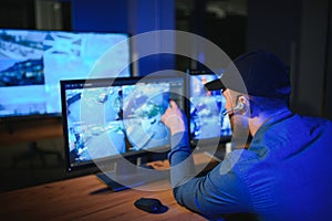 Rear view of security system operator looking at CCTV footage at desk in office