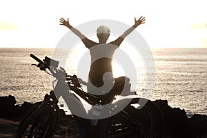 Rear view of senior active woman in front to the ocean at sunset. Black silhouette. Arms raised. Freedon and happiness concept. photo