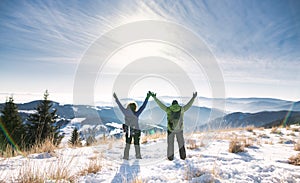 Rear view of senior couple hikers in snow-covered winter nature, stretching arms.