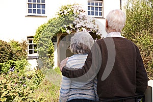 Rear View Of Senior Couple Outside Pretty Cottage