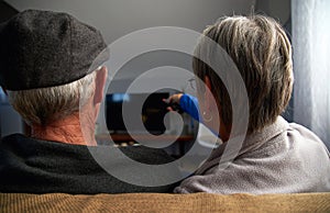 Rear View Of Senior Couple Sitting On Sofa At Home Watching Television Together