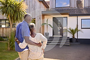 Rear View Of Senior Couple Standing In Driveway In Front Of Dream Home Together