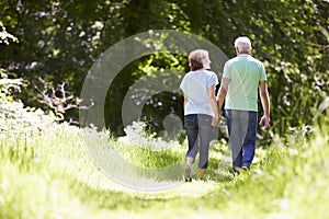 Rear View Of Senior Couple Walking In Summer Countryside