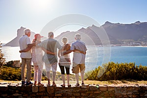 Rear View Of Senior Friends Visiting Tourist Landmark On Group Vacation Standing On Wall