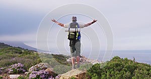 Rear view of senior hiker man standing with his arms wide open standing on a rock