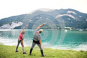 Rear view of senior pensioner couple by lake in nature, doing exercise.