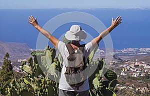 Rear view of senior woman with raised arms traveling in mountain landscape in Tenerife, horizon over the sea - active retired