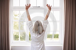 Rear View Of Senior Woman Stretching In Front Of Bedroom Window