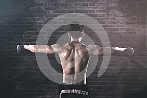 Rear view of shirtless man exercises with dumbbells