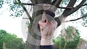 Rear view of shirtless muscular man doing pull up exercise on tree in park