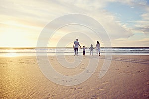 Rear view shot of a carefree family holding hands while walking into the sunset. Mixed race parents and their two kids