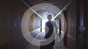 Rear view shot of silhouette of businessman walking with luggage along corridor in hotel