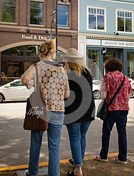 Rear view shot of three women walking together on city street. Female friends out on the street on a summer day