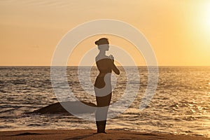 Rear view silhouette slim woman does yoga on tropical sea coast or ocean beach outdoors at sunset