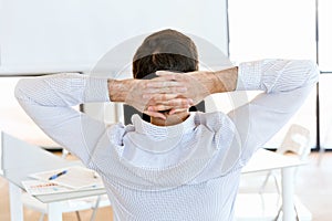 Rear view of sitting businessman with crossed hands on the head