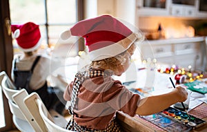 Rear view of small girl and boy indoors at home at Christmas, painting pictures.