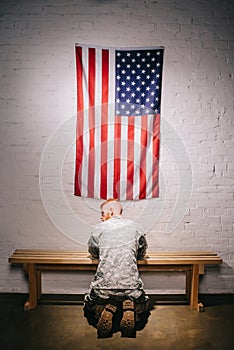 rear view of soldier in military uniform praying with american flag on white brick wall americas independence photo